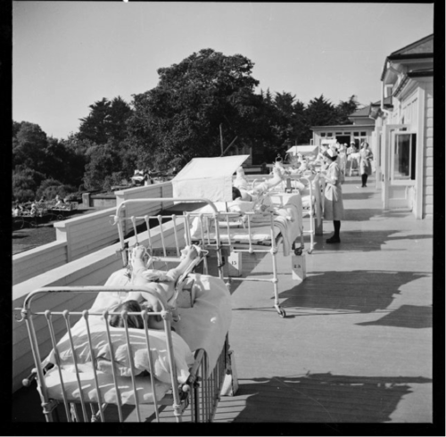 Children on metal hospital beds in the sunshine outside a hospital 